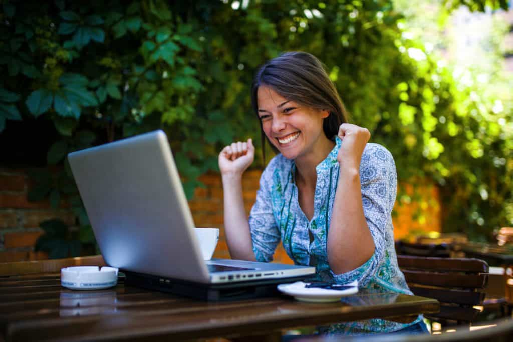 אישה יושבת במקום פסטורלי ולומדת אונליין, דרך המחשב נייד שלה, כאשר נראה שהיא מאושרת ומצליחה במה שהיא עושה